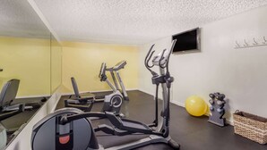 A home gym with exercise equipment, a yellow wall, a mirror, and a TV.