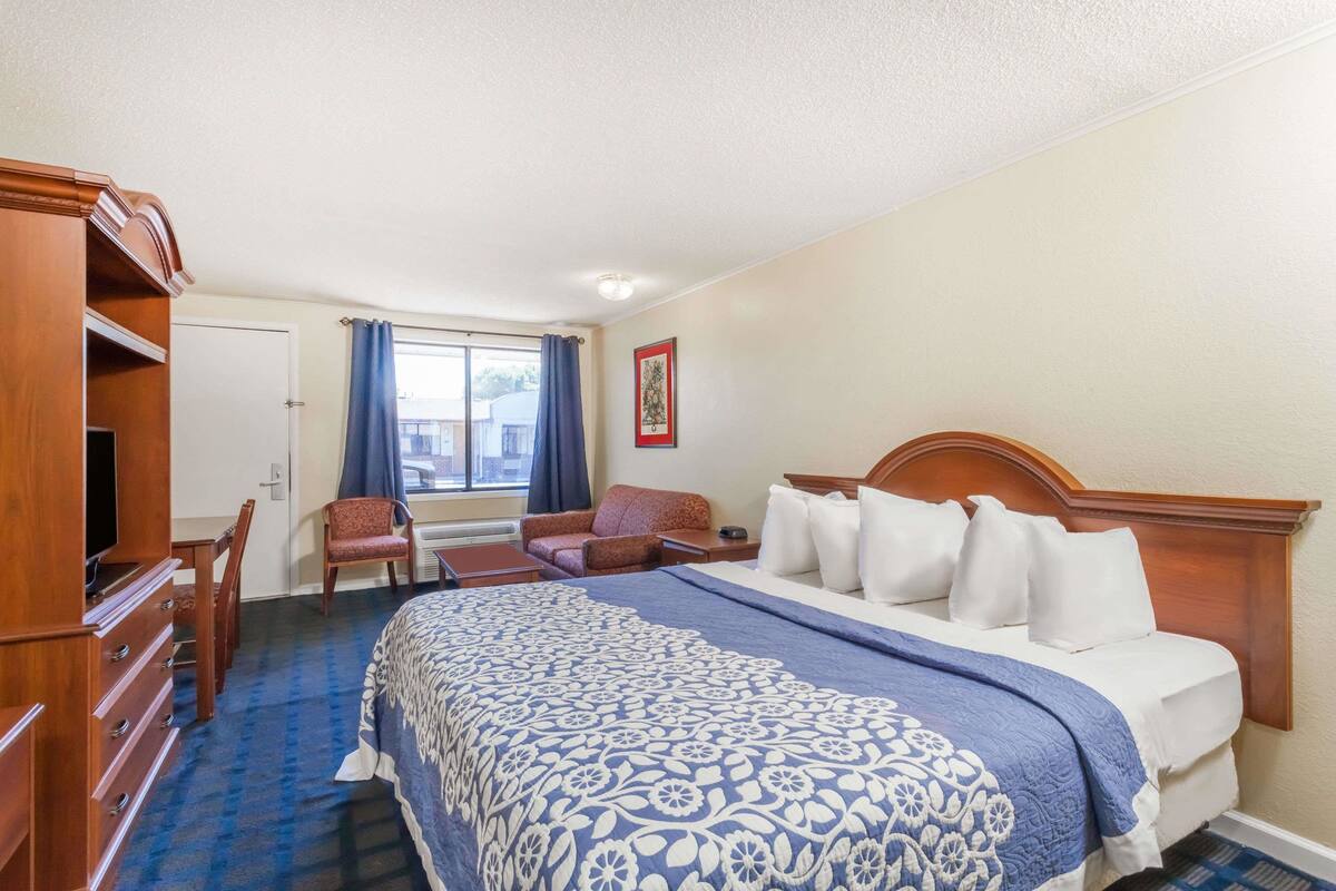 A hotel room with a large bed, a wooden dresser, a desk, and a chair.