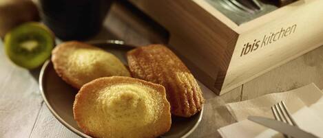 A plate of pastries, a cup of coffee, and a wooden box labeled 'ibis kitchen' on a table.