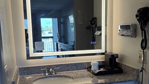 A bathroom with a large mirror, a sink, a hairdryer, and a coffee maker. - Days Inn by Wyndham Ontario Airport (Ontario)