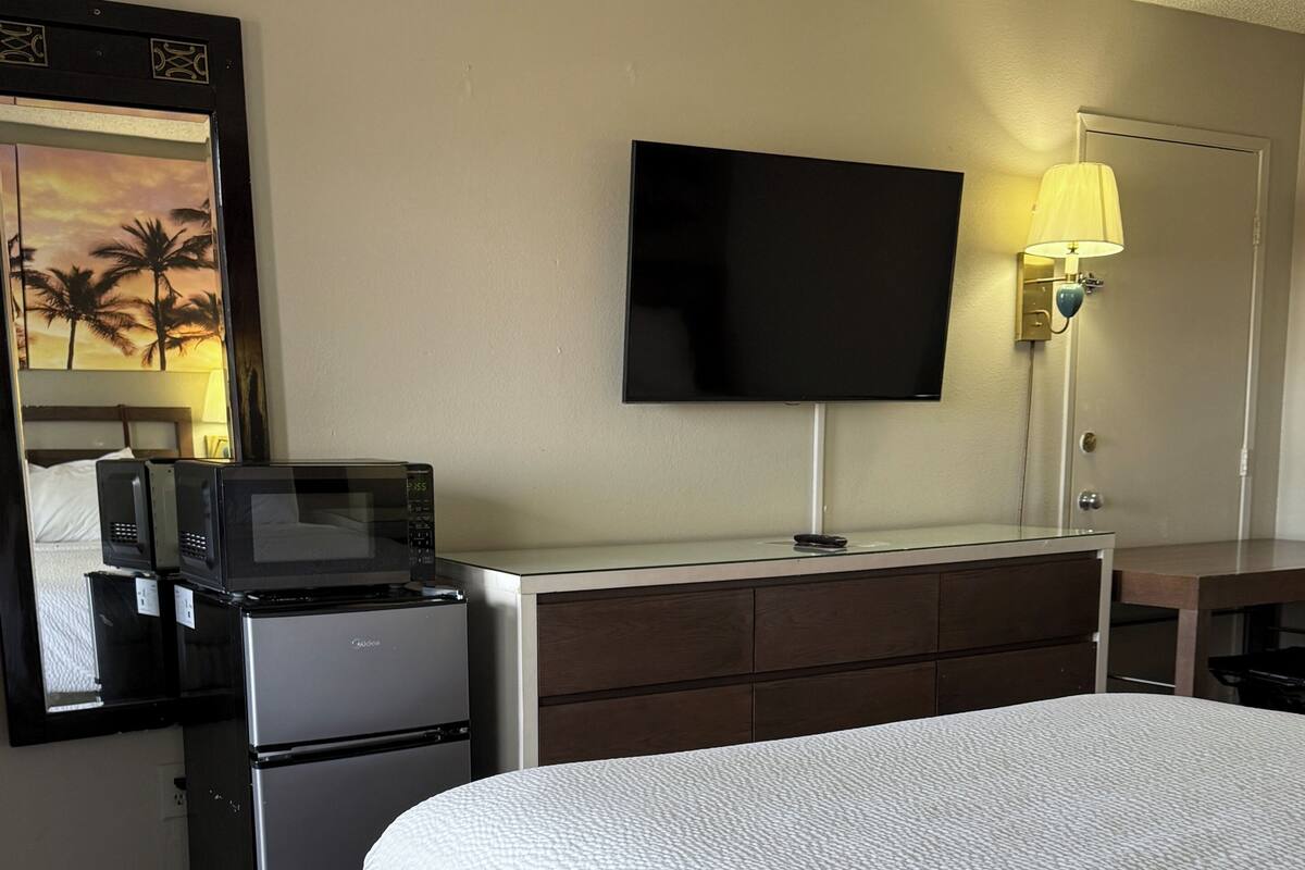 A hotel room with a bed, a flat-screen TV mounted on the wall, a microwave, and a refrigerator.