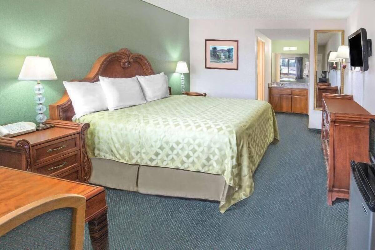 A hotel room with a bed, bedside tables, a desk, a chair, a mirror, a television, and a framed picture on the wall.