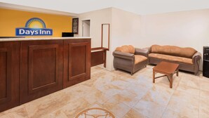 A reception area with a Days Inn sign, a wooden reception desk, a brown leather sofa, and a matching ottoman. - Days Inn by Wyndham Ontario Airport (Ontario)