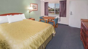 A hotel room with a large bed, a desk with a chair, a small table, and a dresser. - Days Inn by Wyndham Ontario Airport (Ontario)