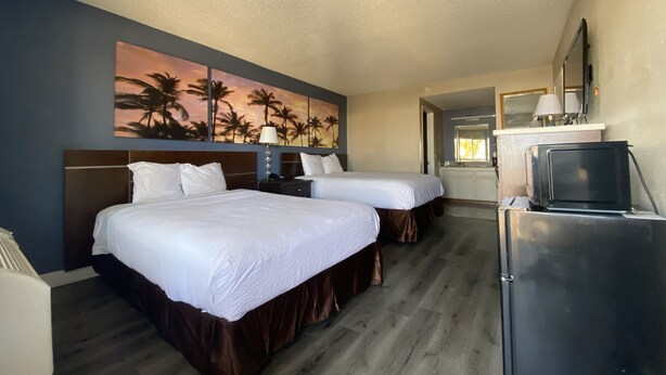 A hotel room with two beds, a painting of palm trees, a kitchenette, and a refrigerator. - Days Inn by Wyndham Ontario Airport (Ontario)