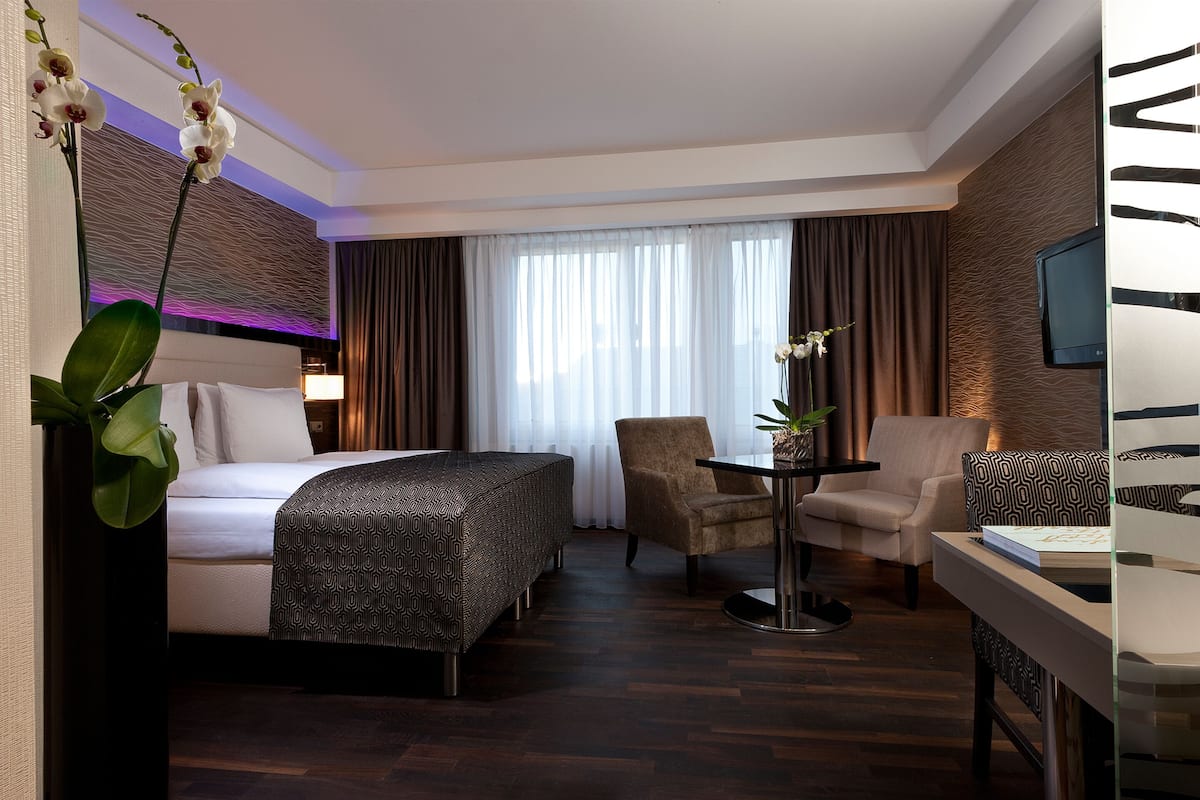 A hotel room with a bed, two armchairs, a small table, and a TV.