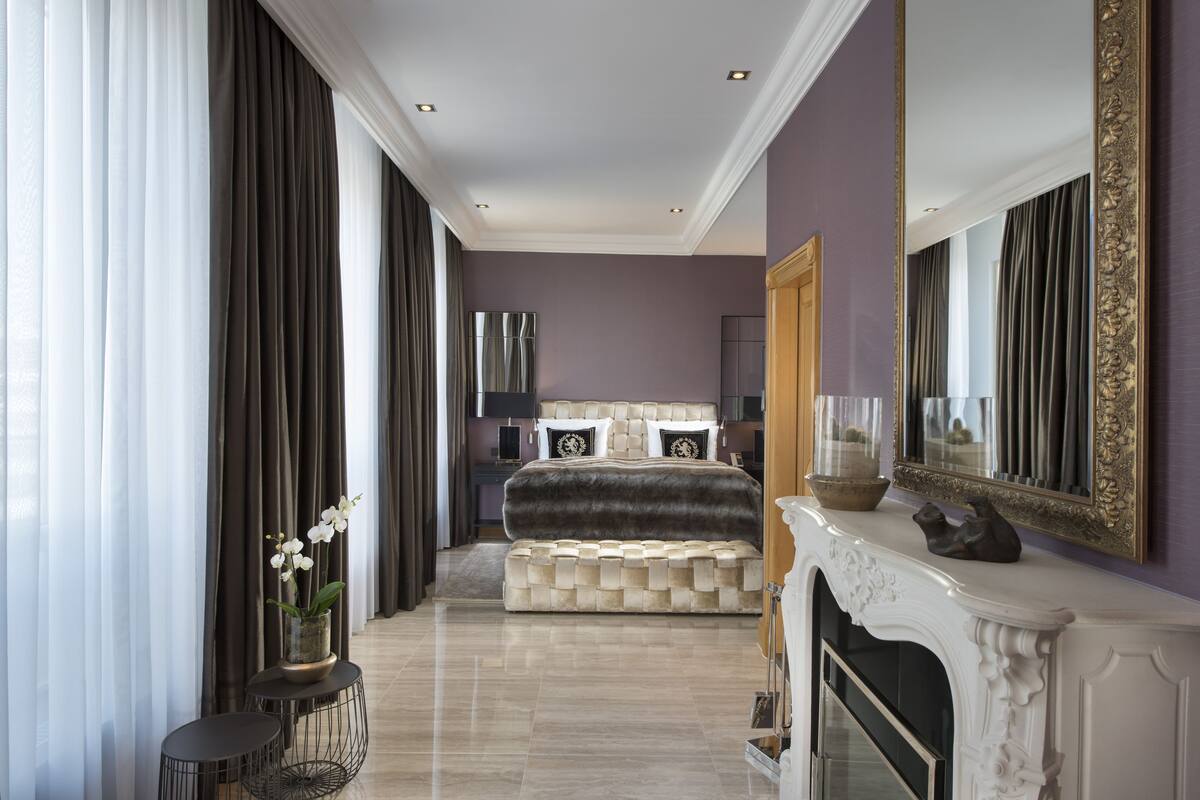 A modern bedroom with a large bed, a fireplace, and a view of the city.