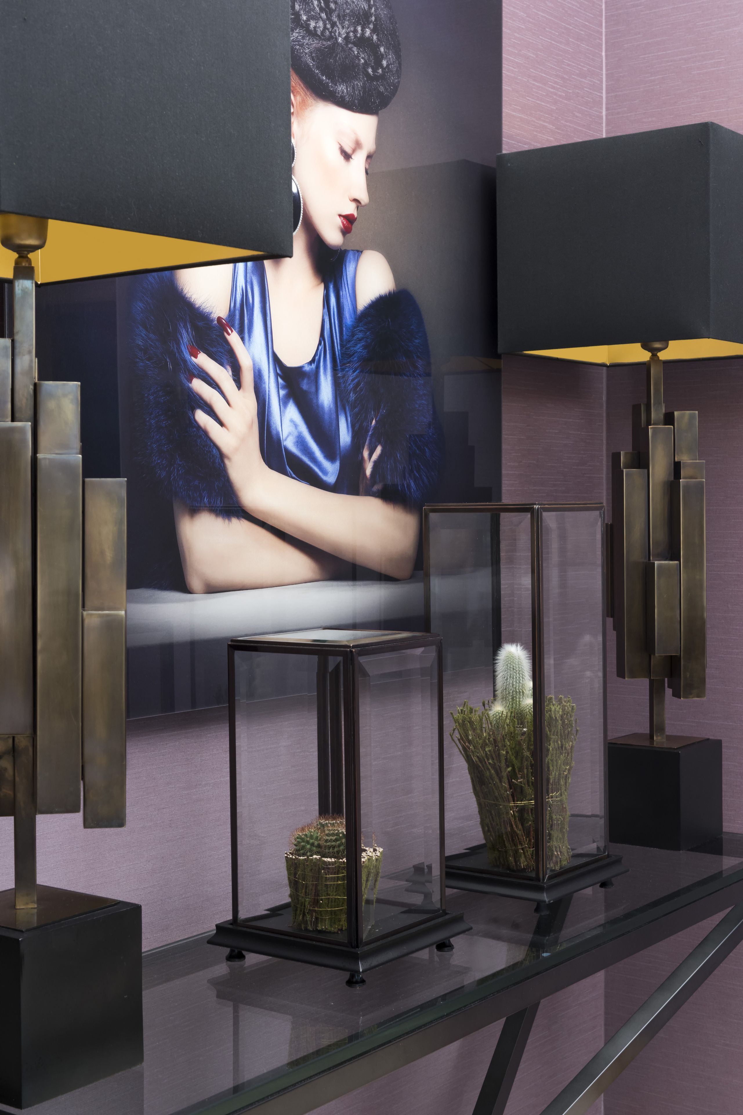 Ein modernes Interieur mit einem großen Flachbildfernseher an der Wand, einem Glastisch mit zwei dekorativen Kakteen und einer minimalistischen Lampe.