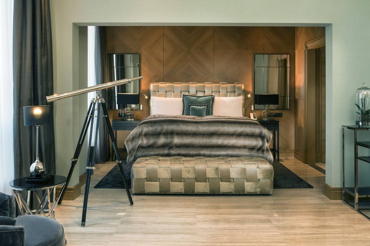 A modern bedroom with a large bed, a side table, a lamp, and a mirror.