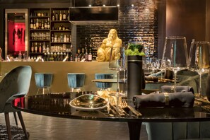 Una zona de bar con una mesa negra preparada para comer, una estatua dorada grande y estanterías llenas de botellas y vasos.