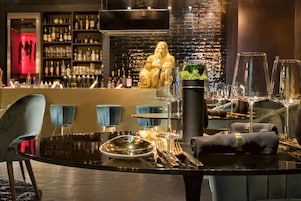 Una zona de bar con una mesa negra preparada para comer, una estatua dorada grande y estanterías llenas de botellas y vasos.