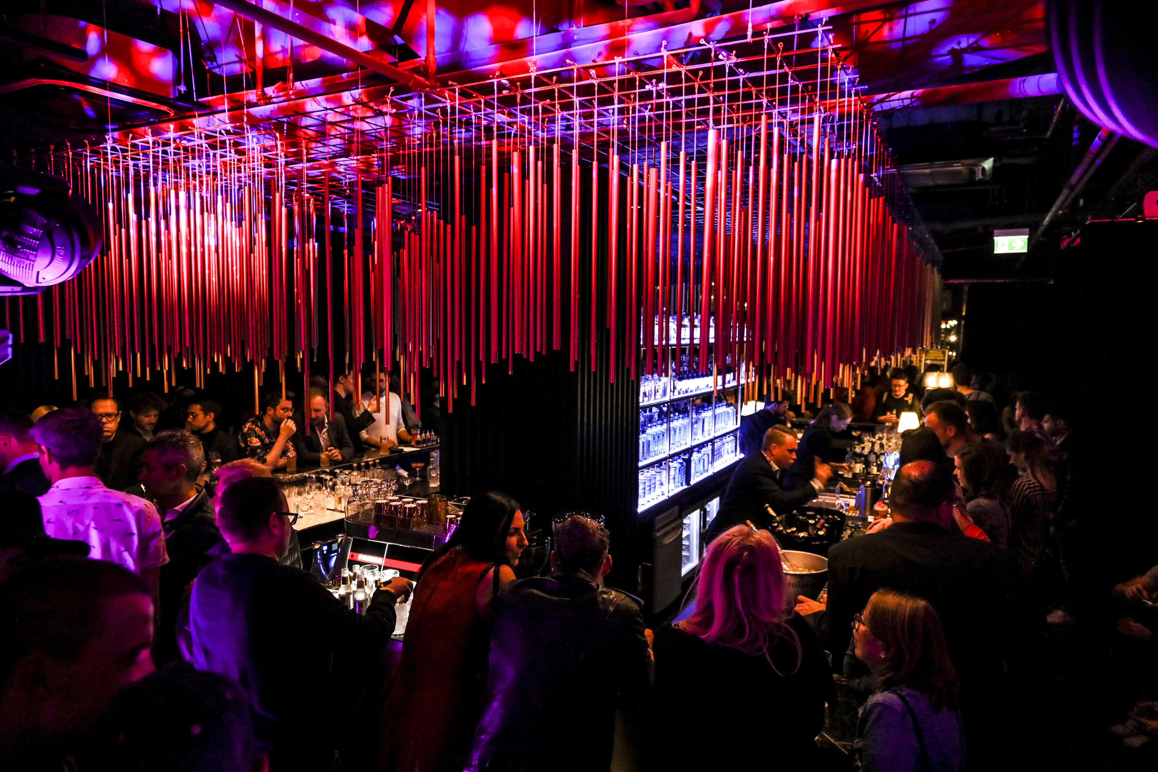 A crowded bar with vertical light fixtures and a bar counter.