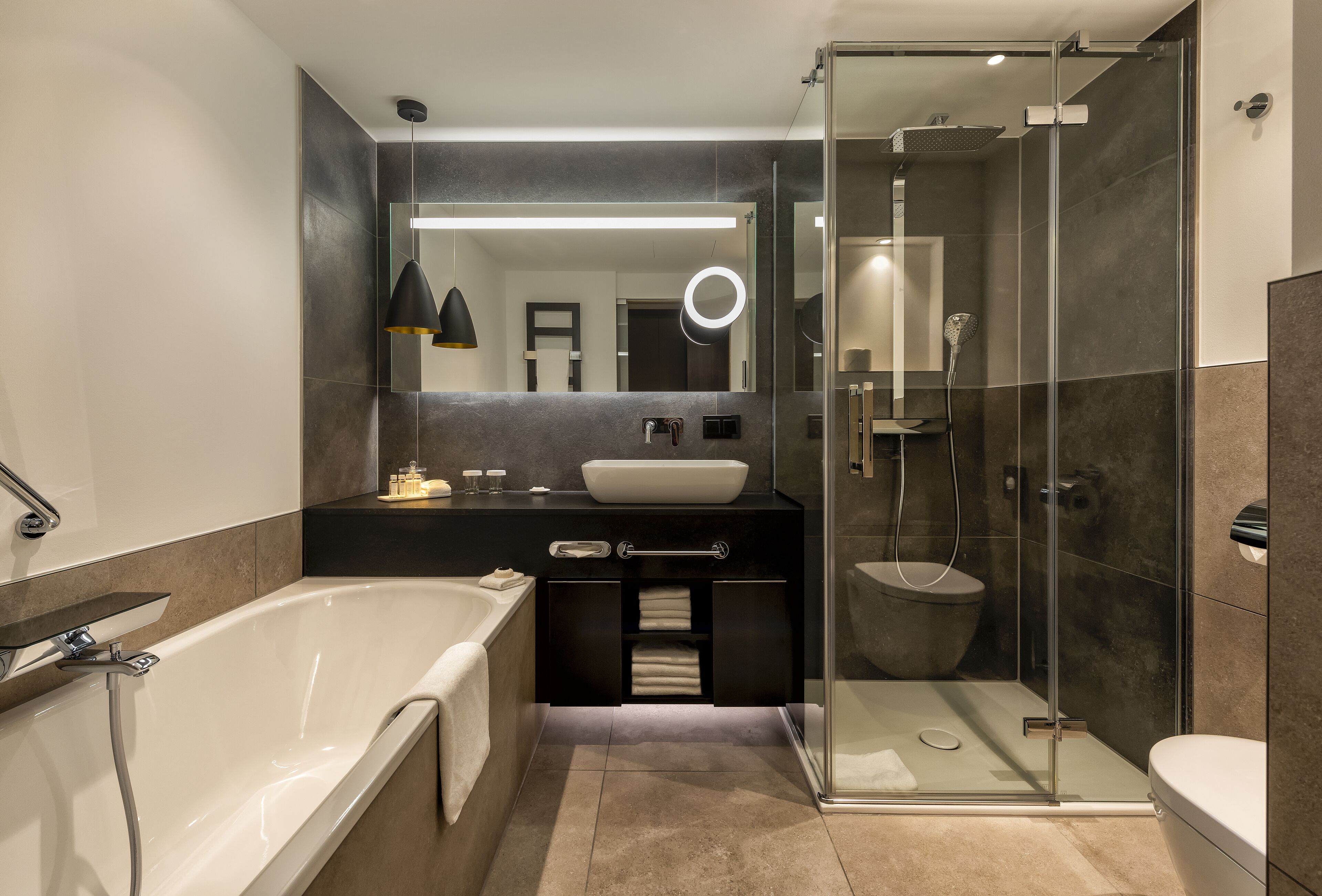 Ein modernes Badezimmer mit einer freistehenden Badewanne, einer Duschkabine und einem Waschtisch mit großem Spiegel und Pendelleuchten.