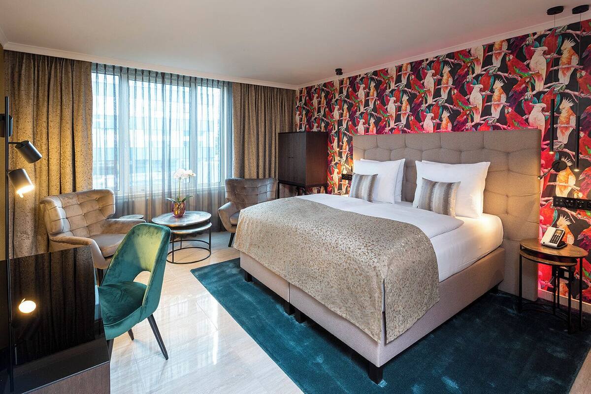 A modern hotel room with a large bed, a sofa, a chair, a small table, and a TV.