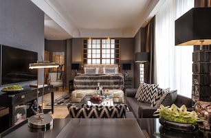 Una sala de estar moderna con sofá, mesa de centro y televisor. Cuenta con un ventanal con persianas, una chimenea y una estantería.
