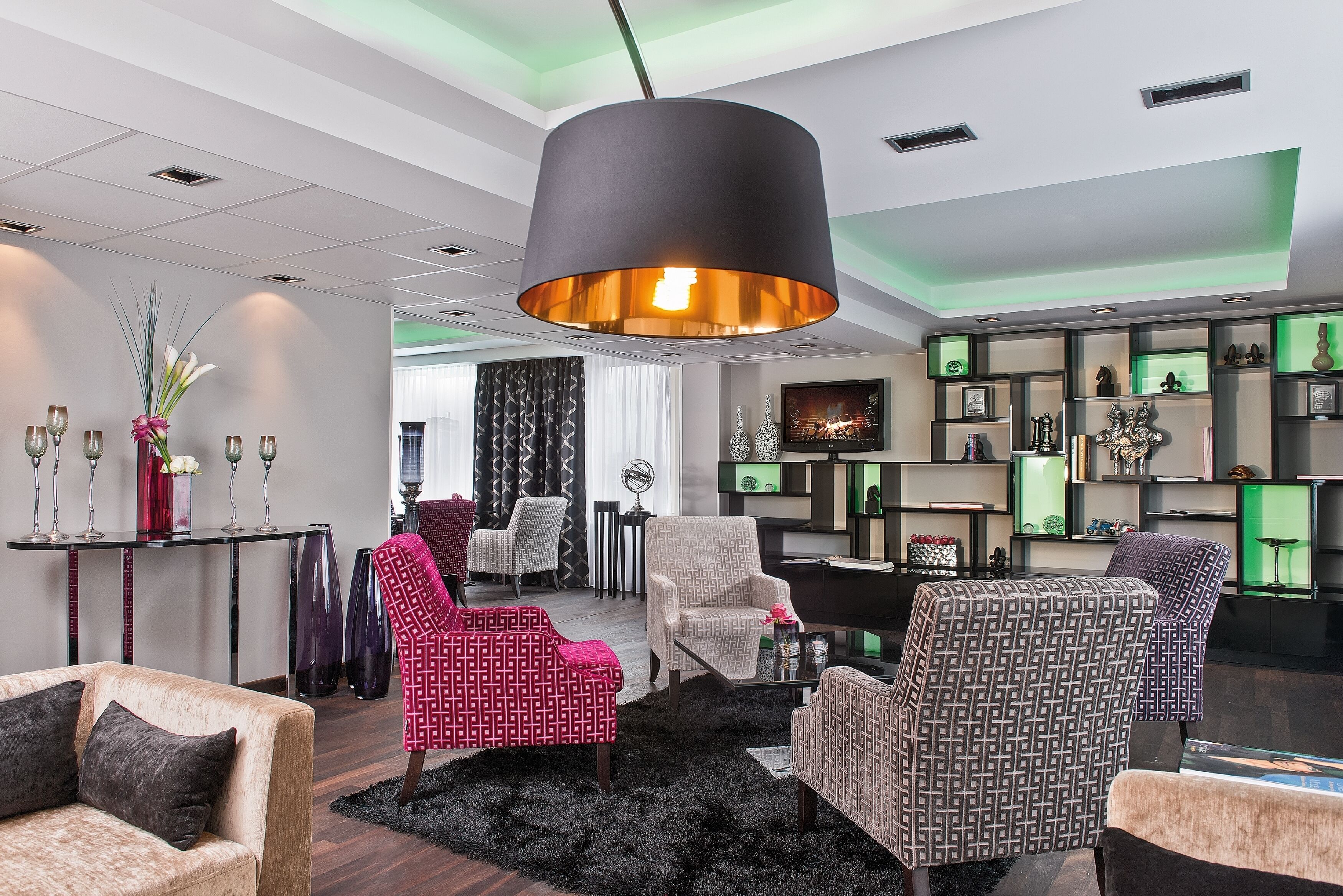A modern living room with a large black pendant light, patterned armchairs, a sofa, and a black shag rug.