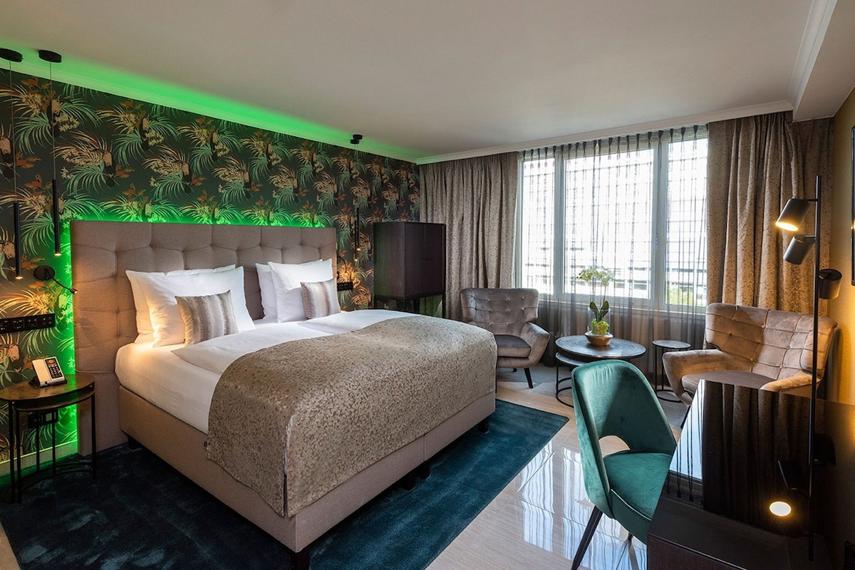 A hotel room with a large bed, a seating area with chairs, a small table, and a television.