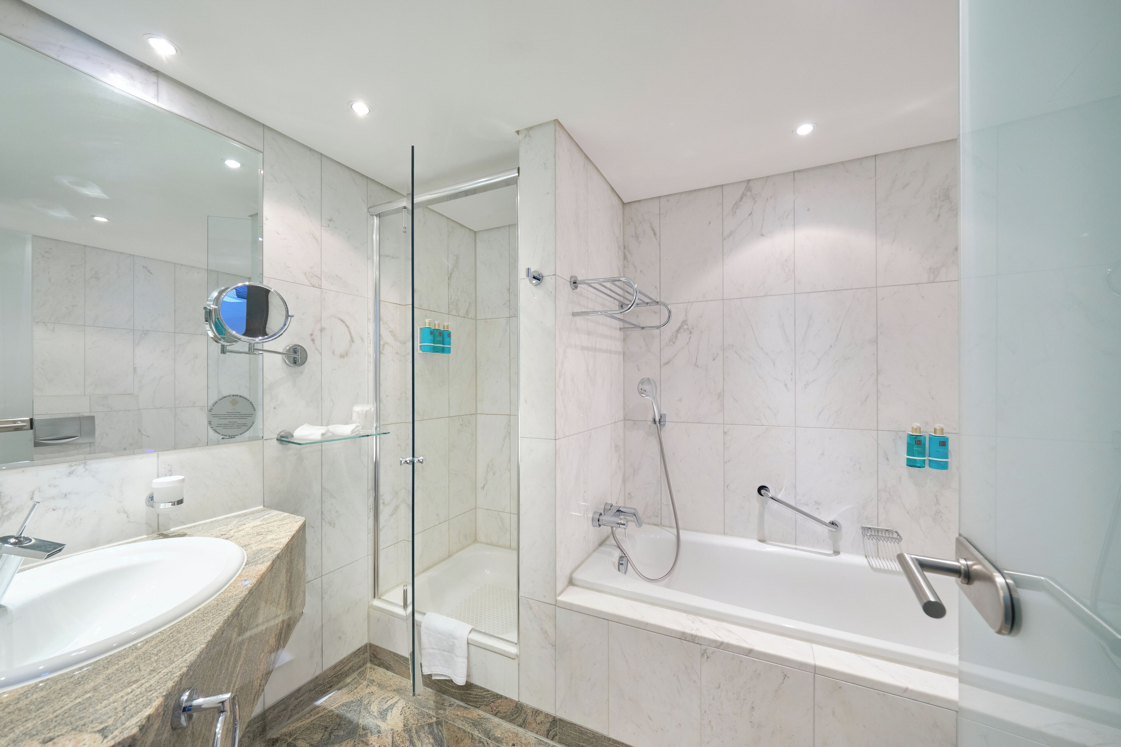 Ein modernes Badezimmer mit einer Glaskabine zur Dusche, einer freistehenden Badewanne und einem Marmor-Waschtisch mit Waschbecken.