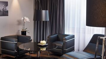 Habitació d'hotel moderna amb un sofà de pell negra, una taula de cafè rodona i un armari de seients negre. Hi ha una catifa negra al terra, una làmpada negra i un vas amb flors blanques sobre la taula de cafè.