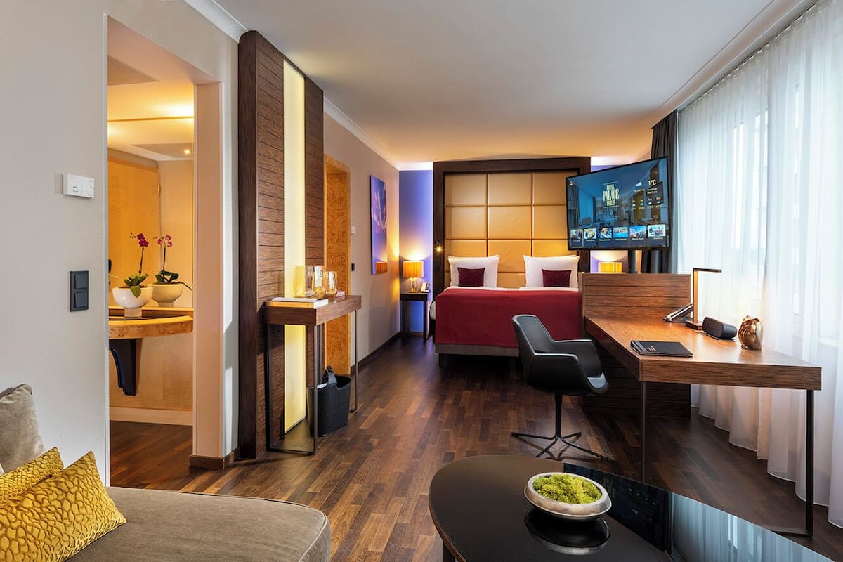 A hotel room with a bed, desk, chair, TV, and a small kitchen area.