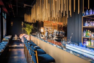 Angolo bar con un lungo bancone, sgabelli da bar e una scaffalatura piena di bottiglie.