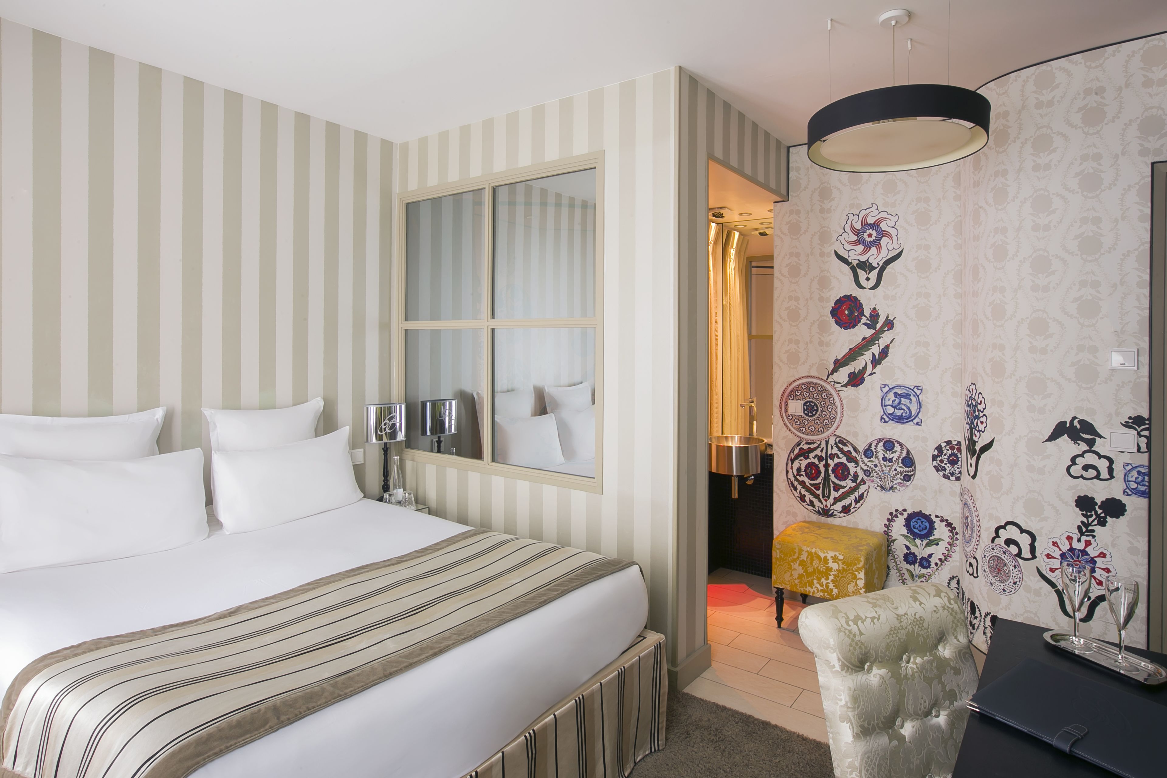 A hotel room with a large bed, a mirror, a small table, and a chair.