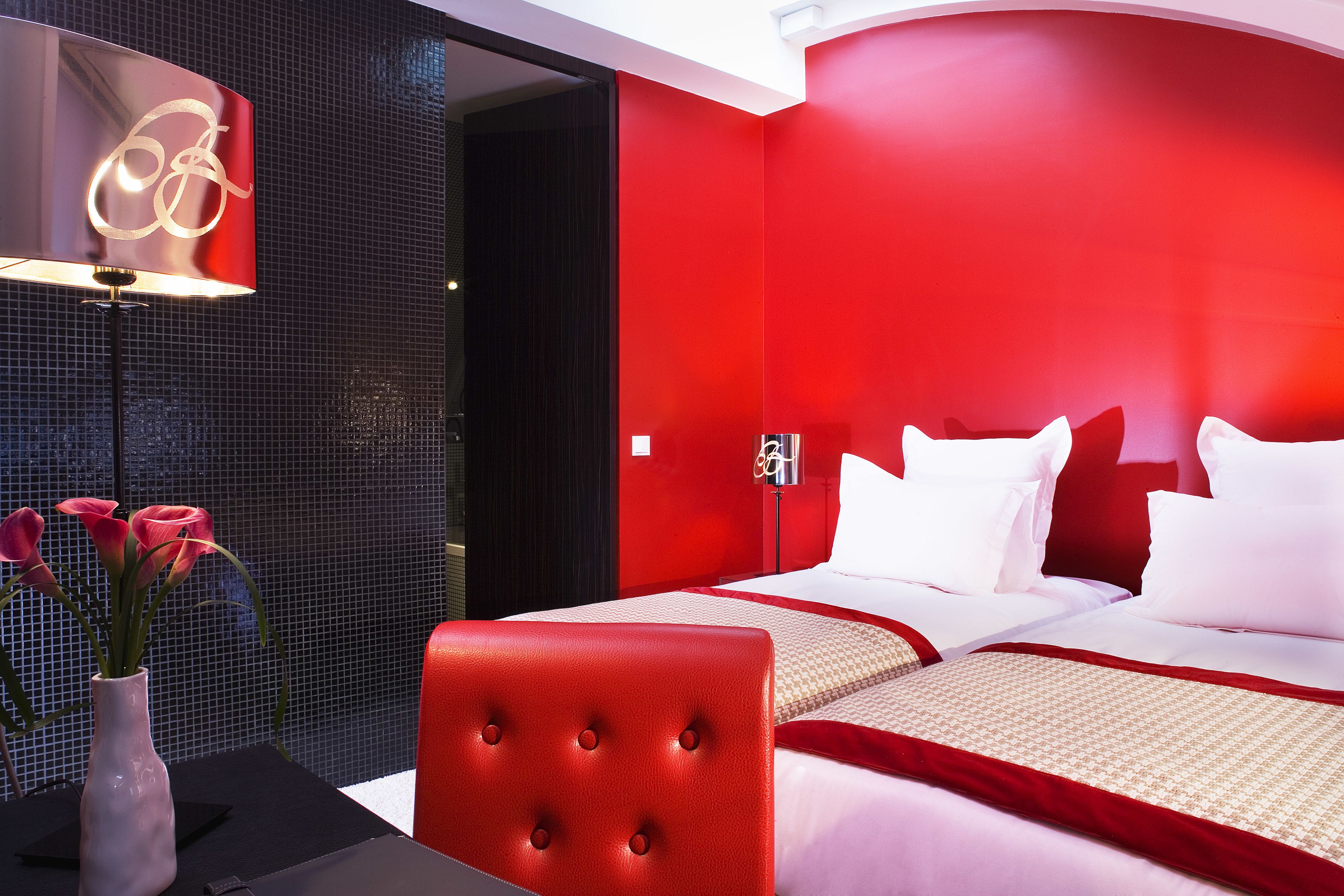 A hotel room with a red and black color scheme, a bed with white bedding, a red headboard, and a vase with flowers on a table.