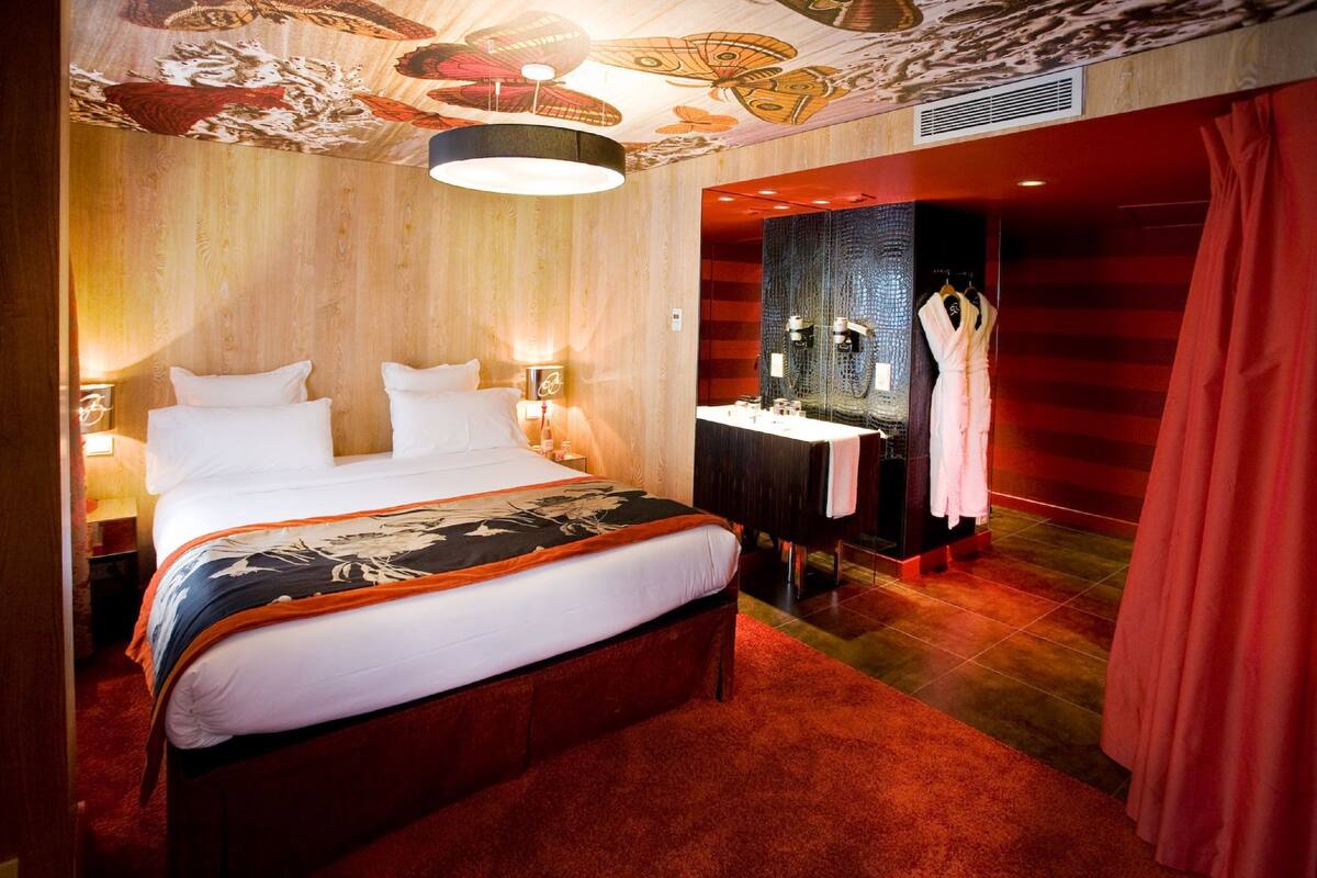 A modern hotel room with a large bed, a vanity with a mirror, and a red curtain.