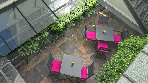 Una terraza en la azotea con mobiliario exterior, barandilla de cristal y plantas.