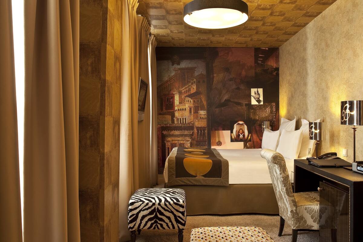 A hotel room with a bed, a desk, a chair, and a large painting on the wall.
