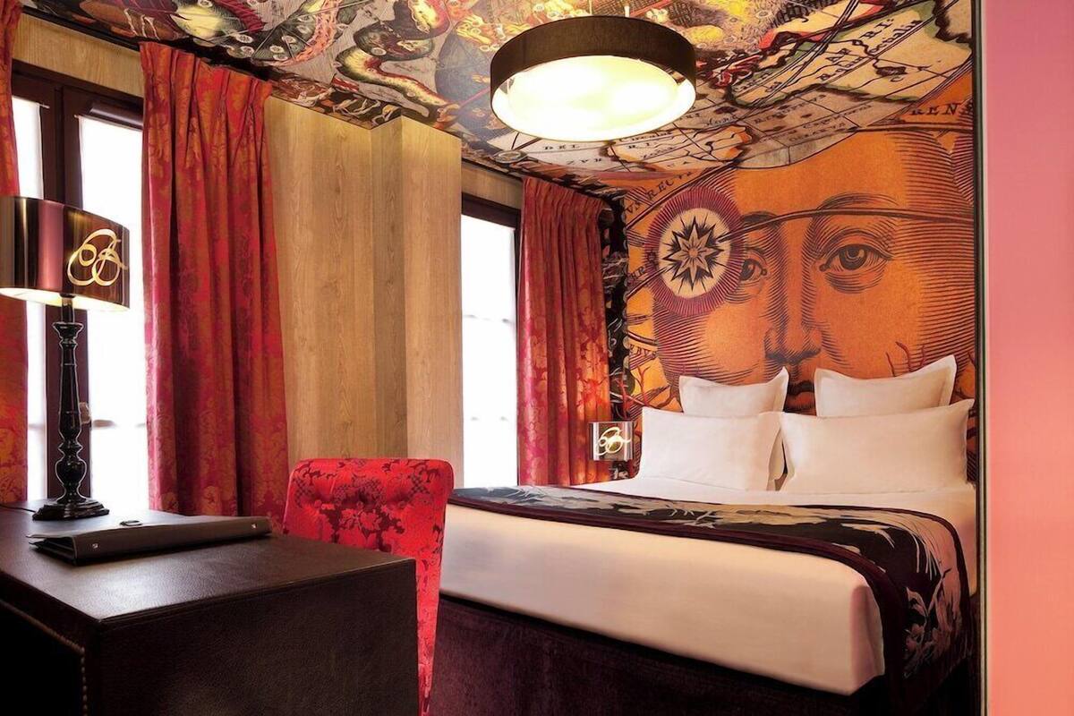 A hotel room with a bed, a desk, a chair, and a map-themed ceiling.
