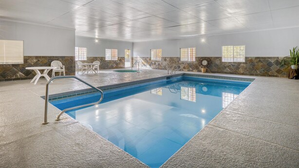 An indoor swimming pool with a tiled floor, a pool ladder, and a seating area with chairs and a table. - SureStay Plus by Best Western Montrose (Montrose)