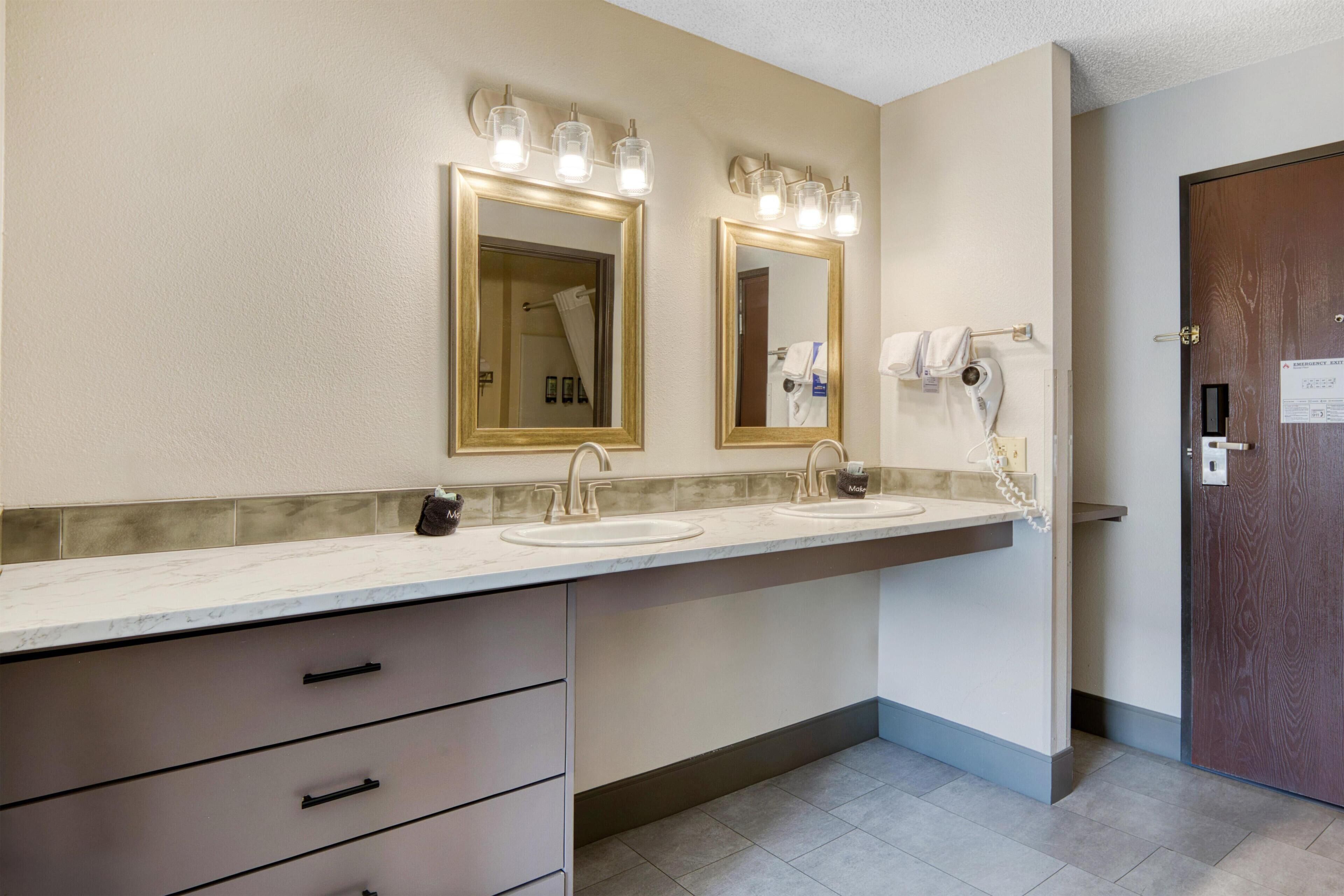 A bathroom with two sinks, a vanity with drawers, and a mirror with lights.