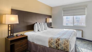 A hotel room with a large bed, two bedside tables with lamps, a window with blinds, and a view of buildings outside.
