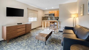 A modern living room with a flat-screen TV, a wooden cabinet, a coffee table, a leather sofa, and a kitchen area with wooden cabinets and a microwave. - SureStay Plus by Best Western Montrose (Montrose)