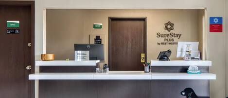 A hotel reception desk with a "SureStay Plus by Best Western" sign, a "Cashier on Duty" sign, a "New Card" sign, and a "Welcome" sign on a dog-shaped decoration.