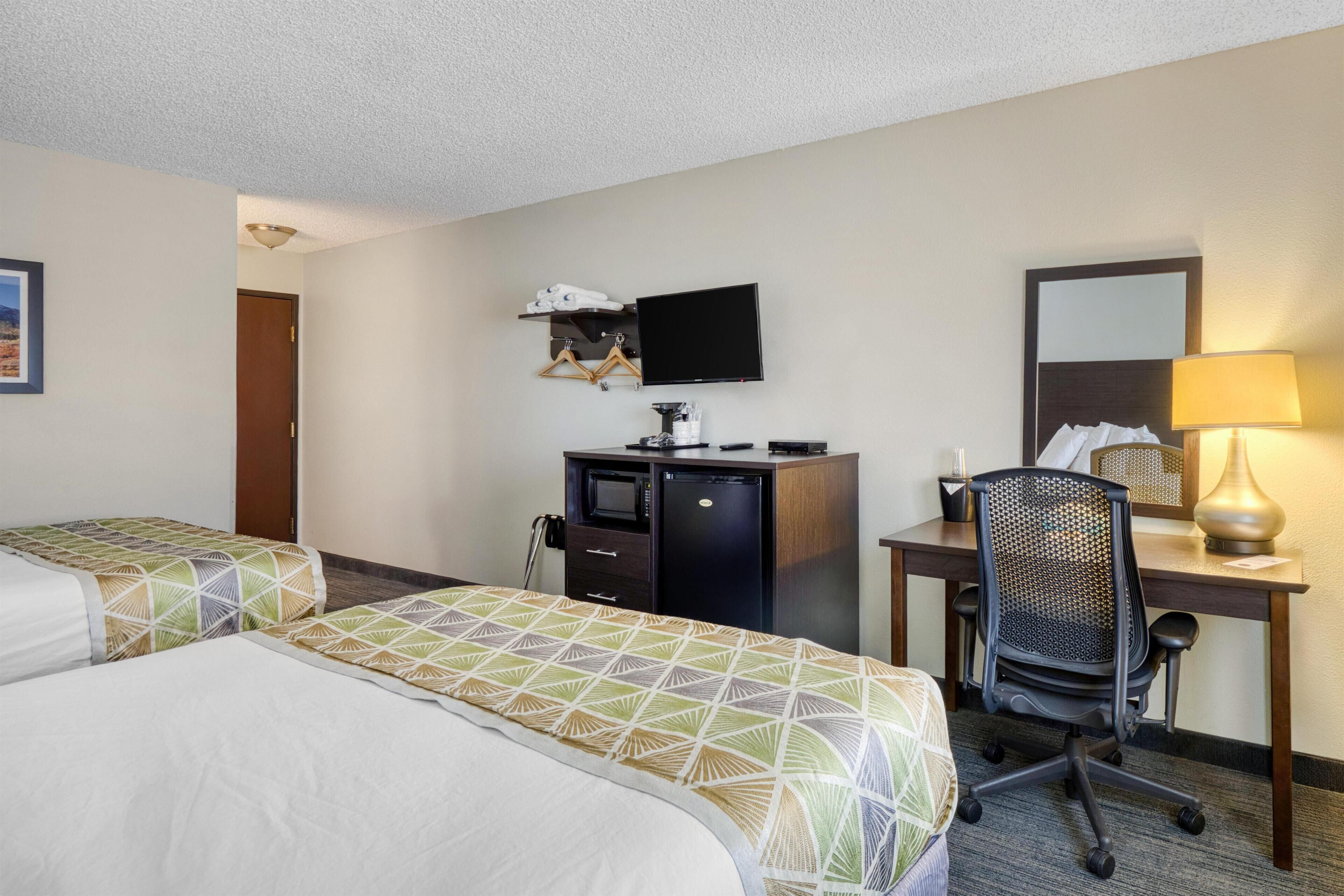 Habitación de hotel con dos camas, un escritorio con computadora, un televisor y una lámpara de escritorio.