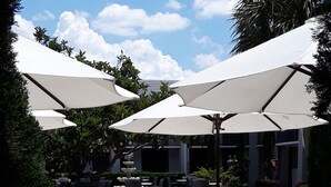 An outdoor patio area with tables and chairs under large umbrellas, surrounded by greenery and a clear sky. - Clarion Inn & Suites Across From Universal Orlando Resort (Orlando)
