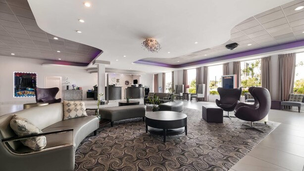 A modern hotel lobby with a curved ceiling, a central seating area with sofas and a coffee table, and large windows providing natural light. - Clarion Inn & Suites Across From Universal Orlando Resort (Orlando)