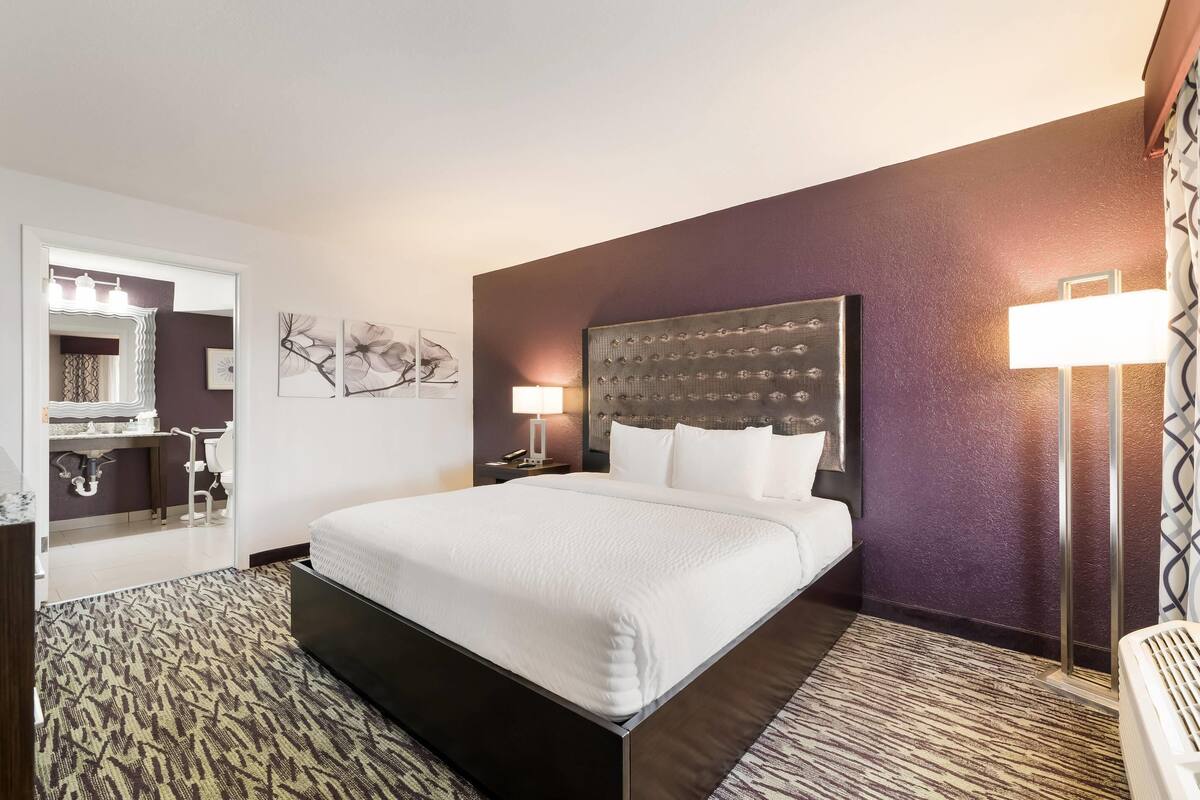 A hotel room with a large bed, a bedside table, a mirror, a headboard, and a floor lamp.