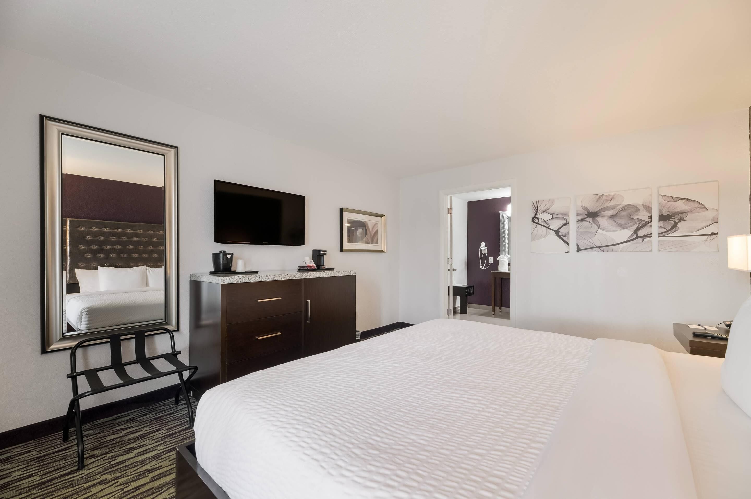 A hotel room with a large bed, a flat-screen TV, a coffee maker, a framed picture, and a door leading to a bathroom.