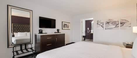 A hotel room with a large bed, a flat-screen TV, a coffee maker, a framed picture, and a door leading to a bathroom.