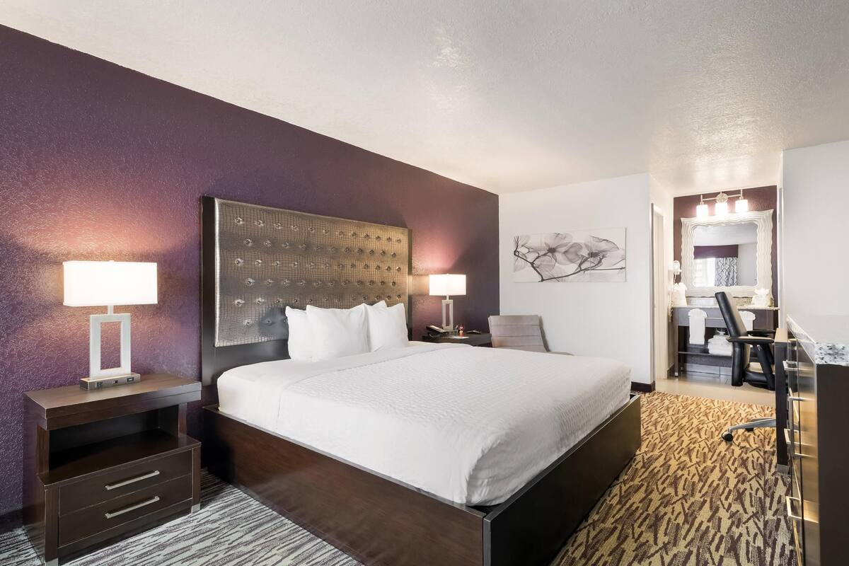 A hotel room with a large bed, two bedside tables with lamps, a desk with a chair, and a mirror.