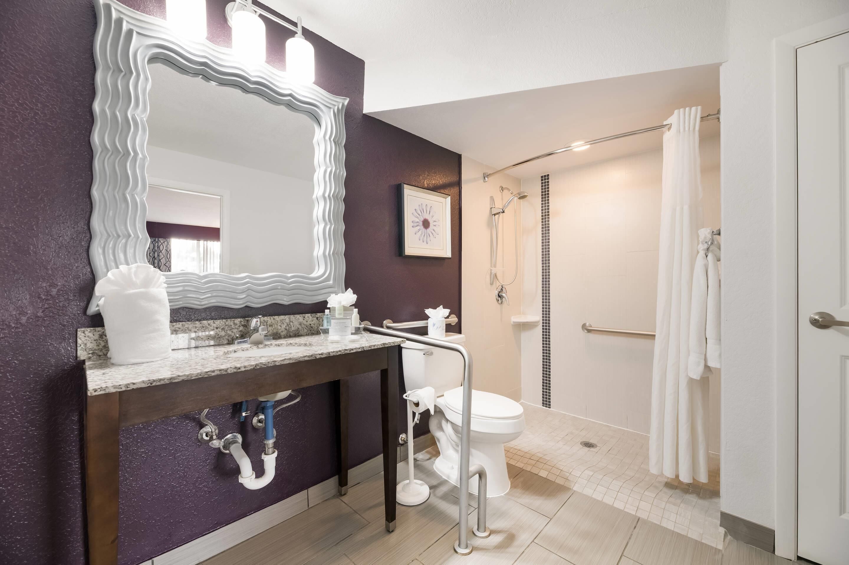 A bathroom with a large mirror, a sink, a toilet, and a shower area.