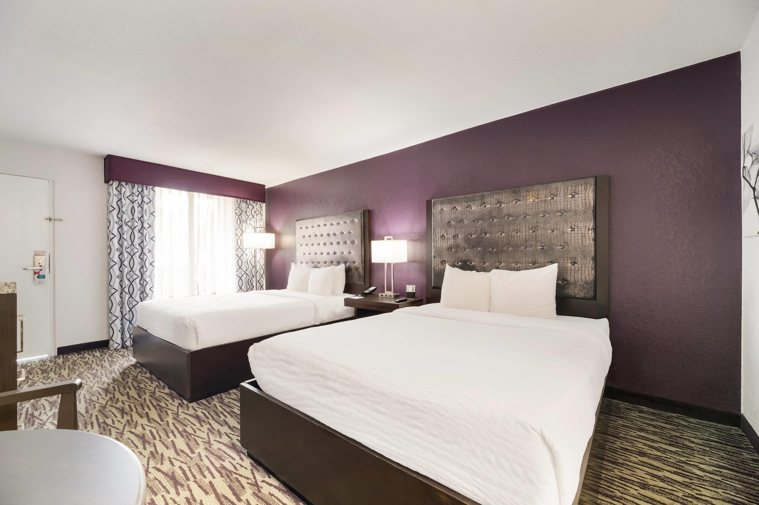 A hotel room with two beds, a desk, and a chair.