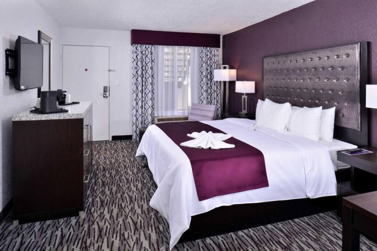 A hotel room with a bed, a desk, a television, a coffee machine, and a window with patterned curtains.