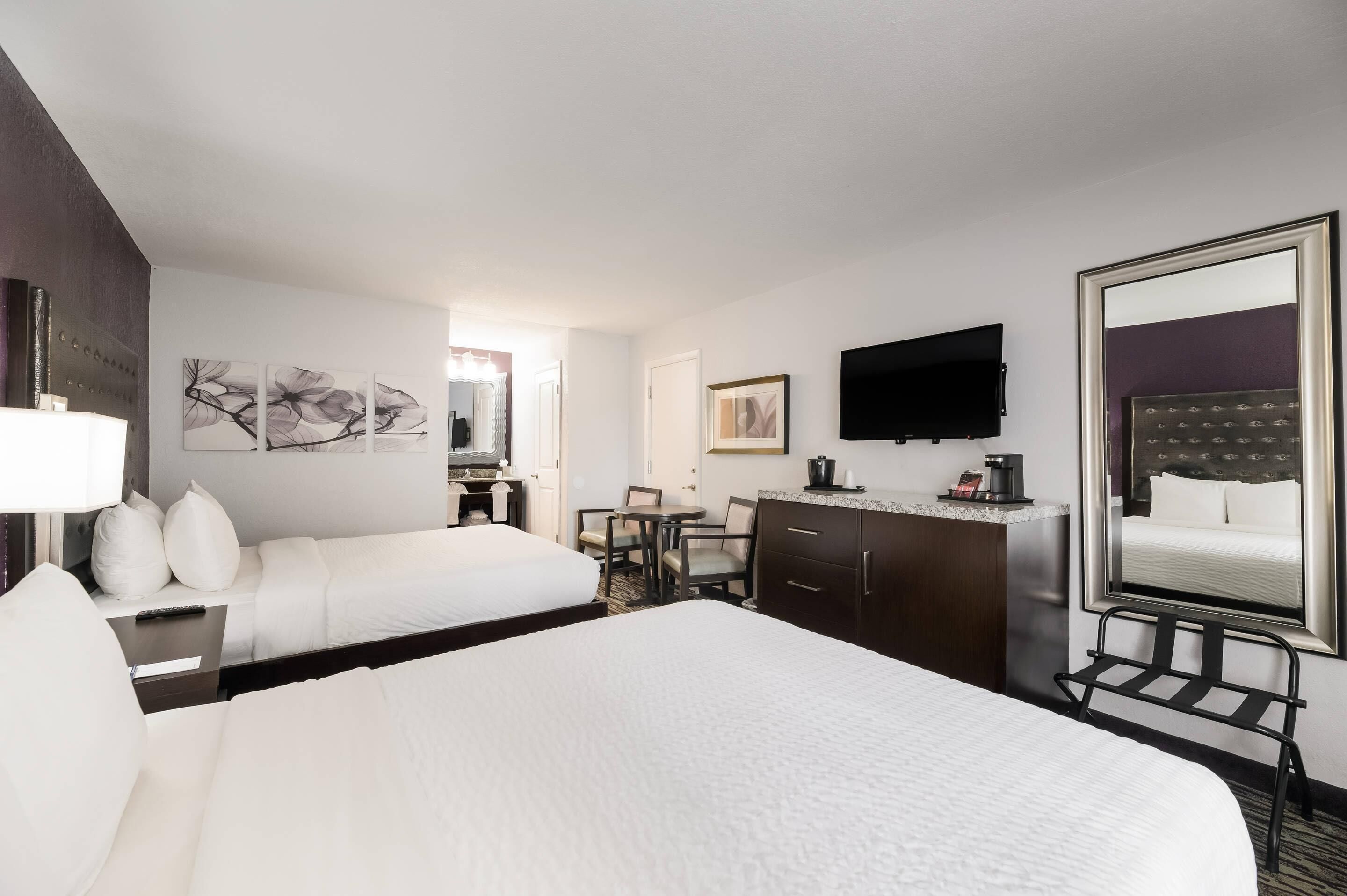 Een hotelkamer met twee bedden, een bureau met stoel, een koffiezetapparaat, een flatscreen-tv en kunstwerken aan de muur.