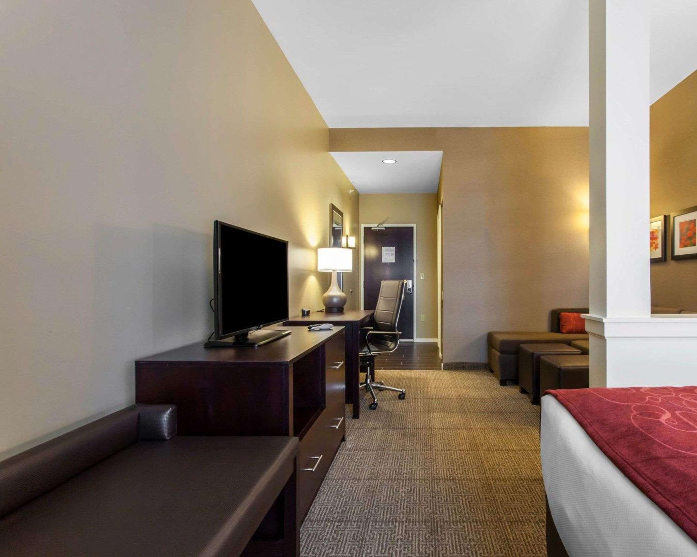 Habitación de hotel con cama, escritorio con televisor, silla, mesita y suelo alfombrado.