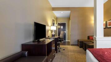 Habitación de hotel con cama, escritorio con televisor, silla, mesita y suelo alfombrado.