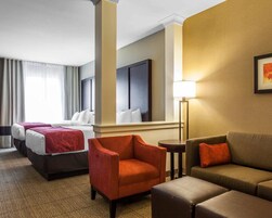 A hotel room with two beds, a sofa, a chair, a lamp, and a framed picture on the wall.